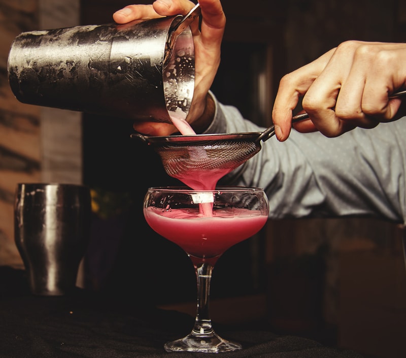 Bartender's hands pouring a cocktail into a class.